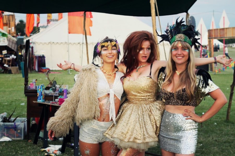 Three women at a festival with gold glitter and sequined outfits